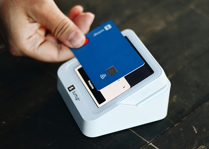 Hand holding a blue contactless card over a white card reader, symbolizing stories of parents disowning their kids.