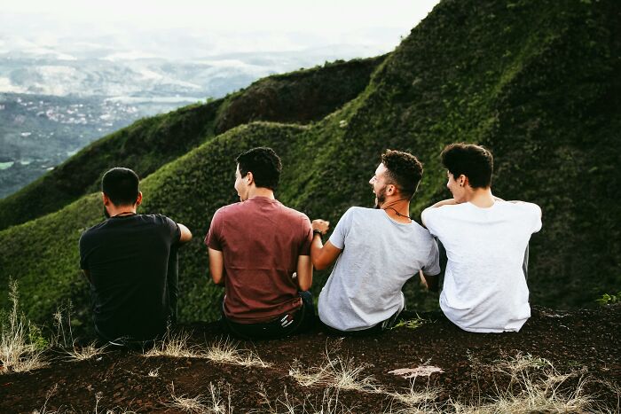 Four young men sitting on a hillside overlooking a valley, engaged in conversation during a red flag poll discussion.