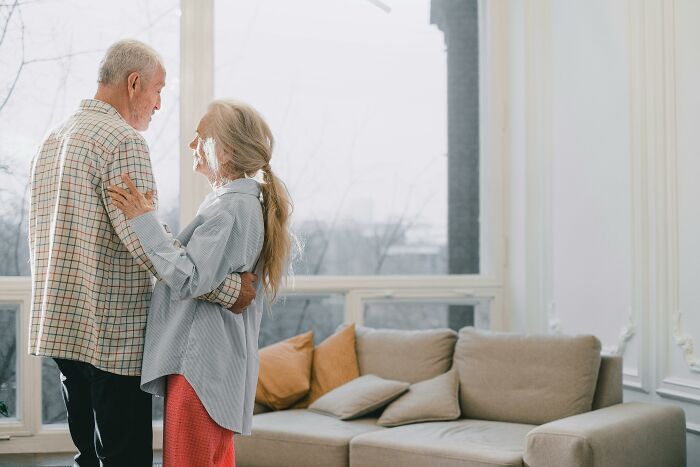 Elderly couple smiling and embracing in a bright living room near large windows, representing connection in Red Flag Poll.