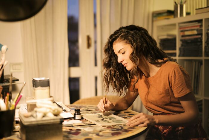 Young woman at a table painting a canvas, focused on her art project in a cozy indoor setting with soft lighting for Red Flag Poll.