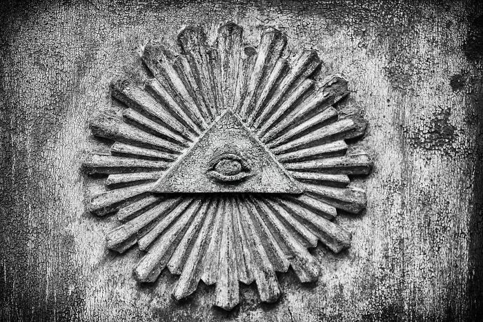 Stone carving of an eye inside a triangle with radiating lines, symbolizing a red flag poll concept.