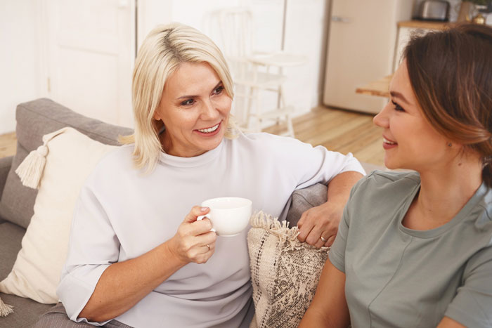 Two women having a friendly conversation on a couch, illustrating neighbor demands and babysitting responsibilities.