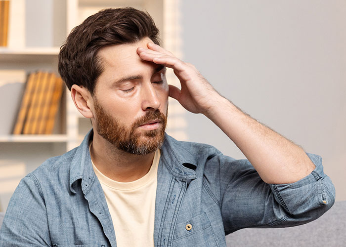 Man looking stressed with hand on forehead, representing refusal to babysit roommate&rsquo;s kid after night shift.