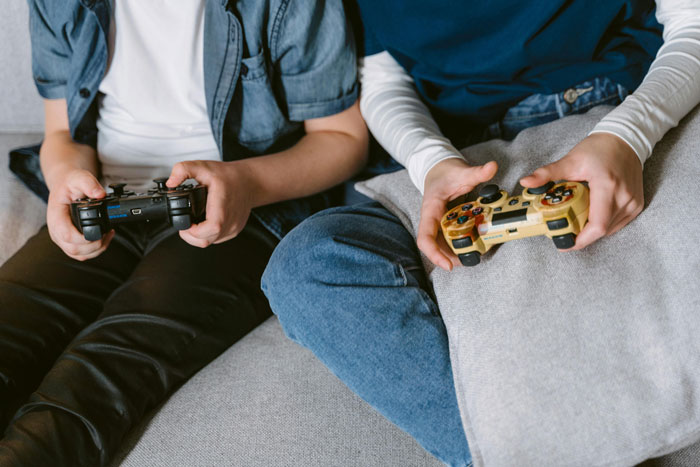 Two young men sitting on a couch playing video games, highlighting bros helping clean and chores conflict. Two young men sitting on a couch playing video games, highlighting bros helping clean and chores conflict.