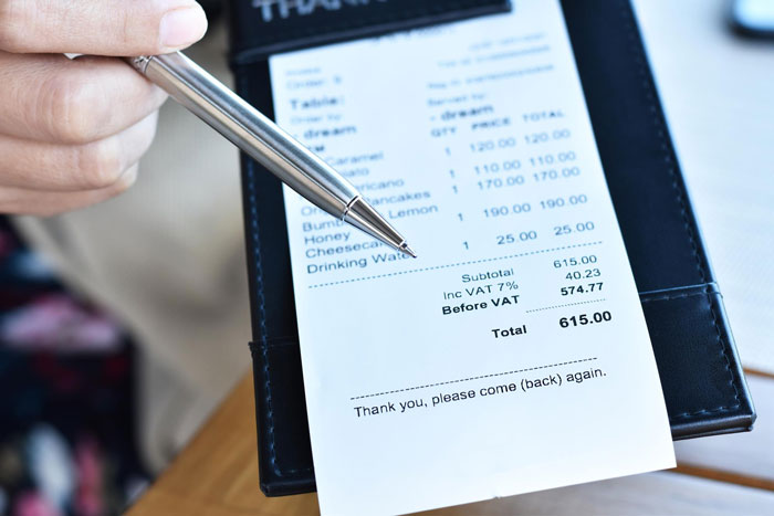 Hand pointing with pen at restaurant bill showing total amount, highlighting friend laughs off vegan paying only for food concept.