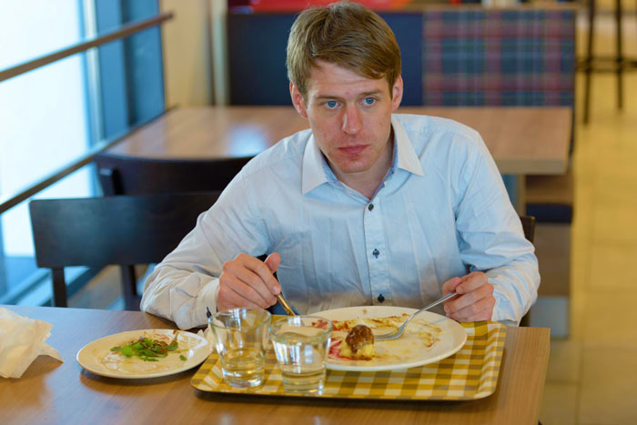 Young man eating alone in a restaurant, reflecting on the vegan&rsquo;s warning about paying only for his food