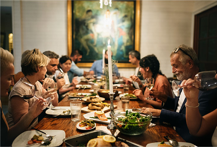 Group of people dining together around a table with food and drinks, capturing a moment of treating the table at dinner.