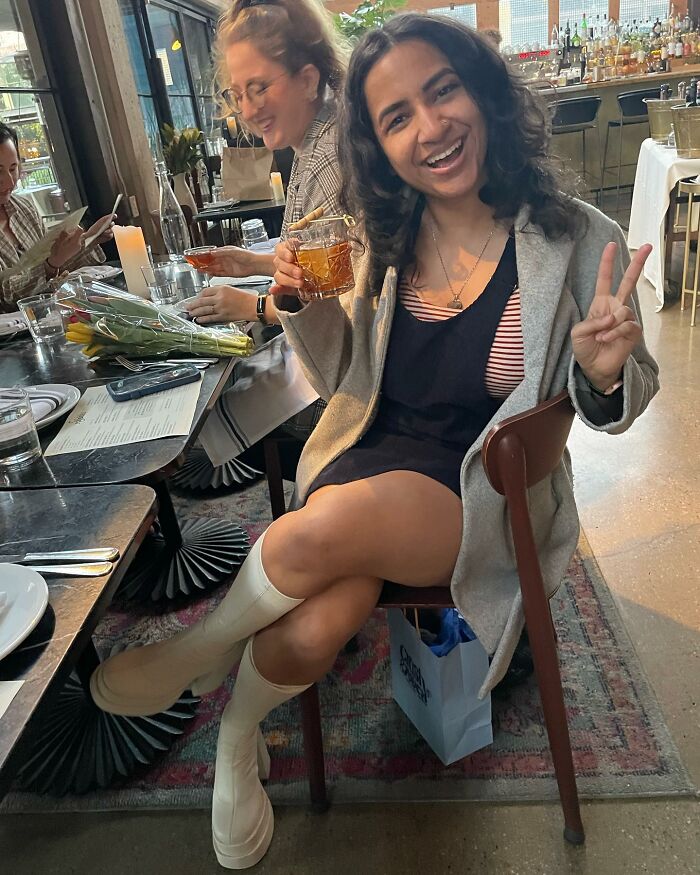 Young woman enjoying tea at a restaurant, smiling and making a peace sign, sharing celebrity gossip vibes.