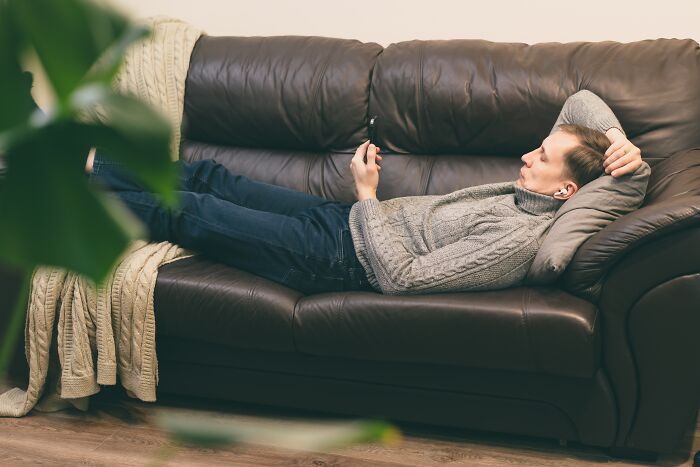 Man lying on a brown leather couch, looking at phone, illustrating people who called off their wedding reasons.