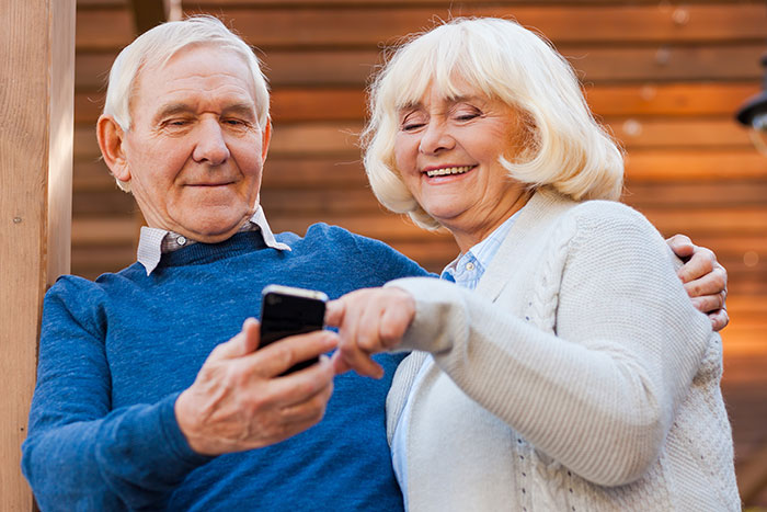 Elderly couple smiling while using a smartphone, symbolizing phone tracking and location sharing with parents.