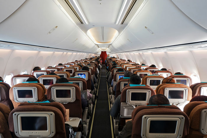 Inside of a commercial flight cabin showing passengers seated during a flight with seatback entertainment screens active.