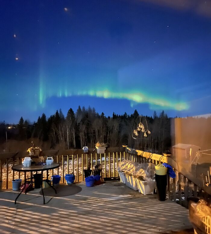 Northern lights glowing over a peaceful backyard deck at night, capturing low-key pleasures and simple happiness.