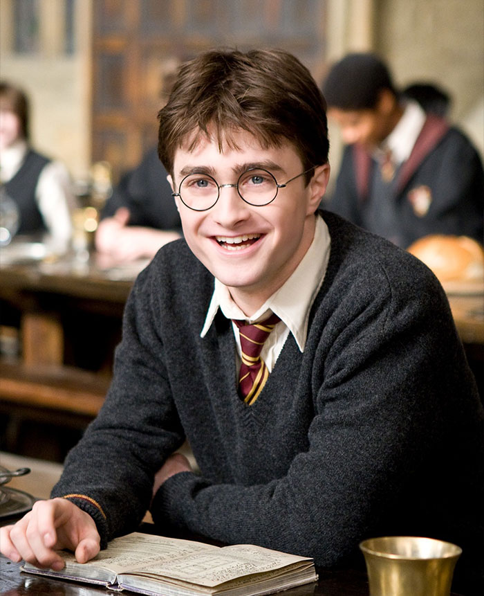 Daniel Radcliffe in school uniform smiling with book open in front, representing richest actor in the world 2025.