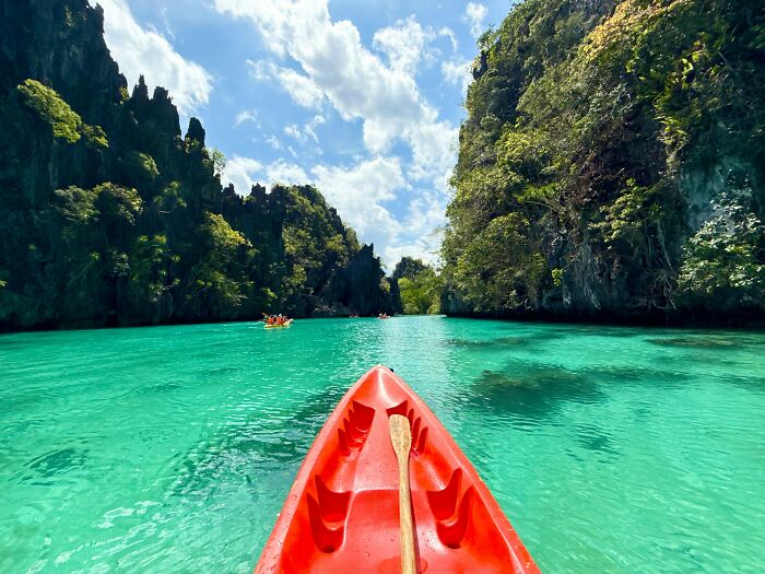 Red kayak paddling through turquoise water surrounded by lush cliffs, showcasing natural wonders full of magic.
