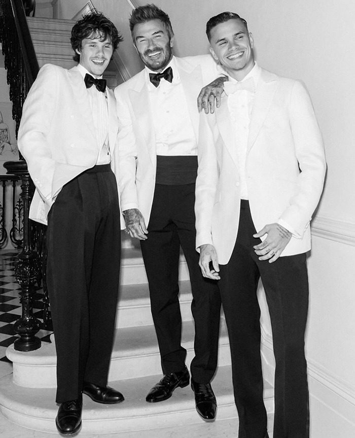 Romeo and Cruz Beckham dressed in tuxedos, posing and smiling on a staircase amid family drama on Instagram.