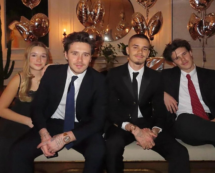 Romeo and Cruz Beckham sitting together in suits at a party with gold balloons in the background amid family drama.