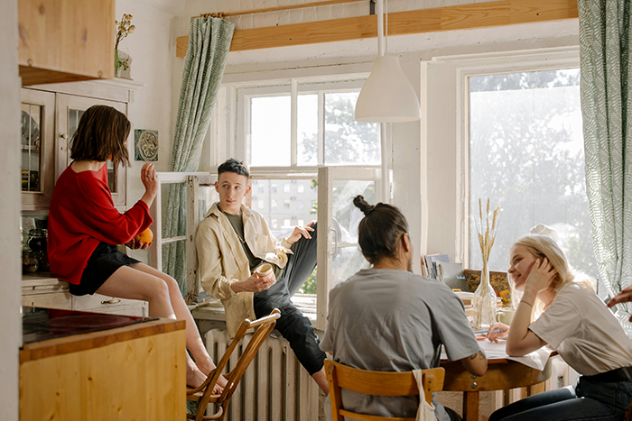 Middle-aged woman with a shopping habit eating and talking with roommates in a bright kitchen during daytime.
