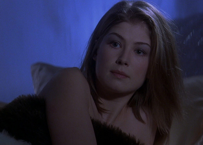 Rosamund Pike in a dimly lit scene, reflecting on her experience with Bond girl auditions and the unzip and drop the dress claim.