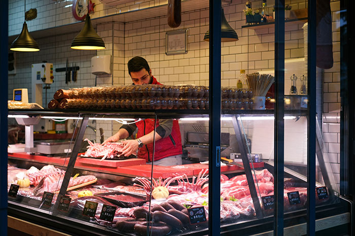 Butcher arranging meat cuts behind a glass display in a shop, showcasing tall and loud customer service approach.