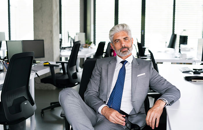 Mature confident man in gray suit sitting in office chair, representing tall and loud comebacks to entitled bosses.