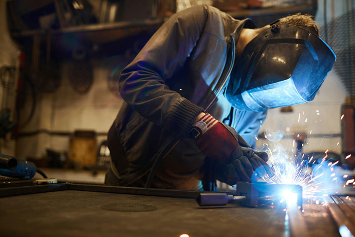 Worker welding metal in a workshop, illustrating strength and presence related to tall and loud personality traits.