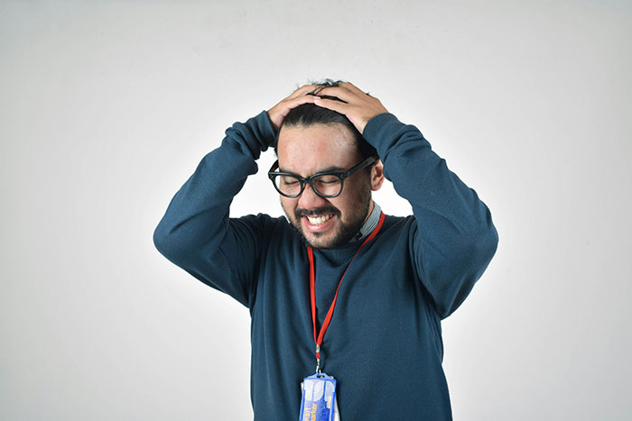 Man with glasses holding his head in frustration wearing a lanyard, representing comebacks to entitled bosses and tall loud presence.