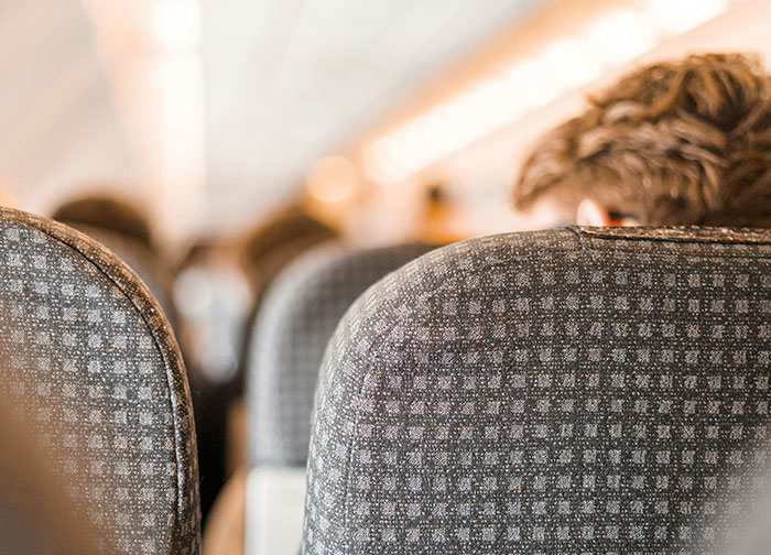 Woman thinks she's right to complain about plane passenger seated on airplane with blurred passengers ahead.