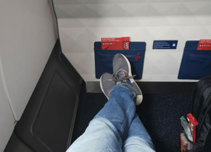 Passenger stretching legs in airplane seat with Delta safety card visible, illustrating plane passenger complaint scenario.