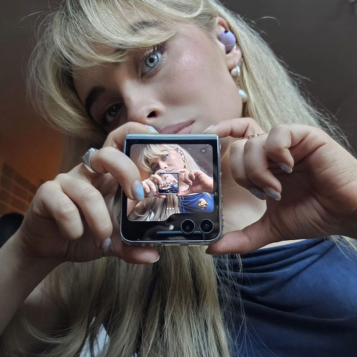 Sabrina Carpenter holding a folding phone showing a recursive photo, highlighting her rising net worth after Espresso success.