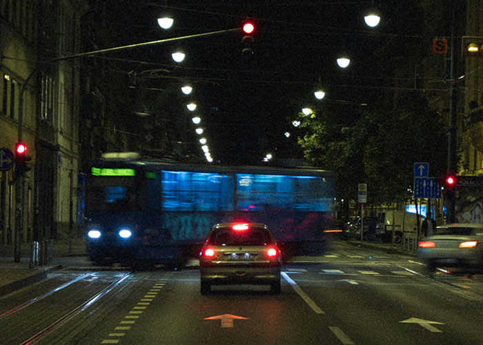 Nighttime city street with a car stopped at a red light and a bus passing by, illustrating urban safety tips for women.