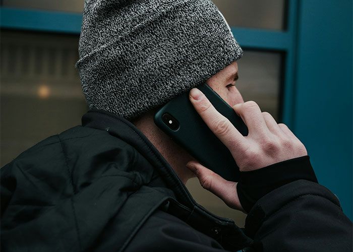Person in a gray beanie and black jacket making a phone call, illustrating safety tips women use today.