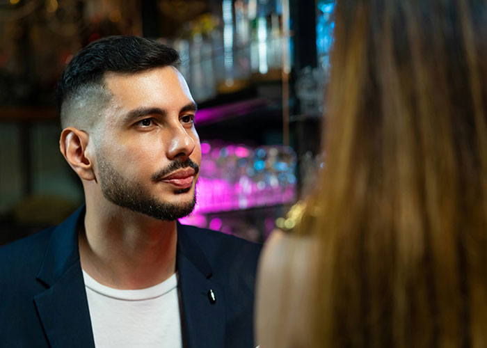 Man in a dark jacket talking to a woman in a bar setting illustrating safety tips women picked up the hard way