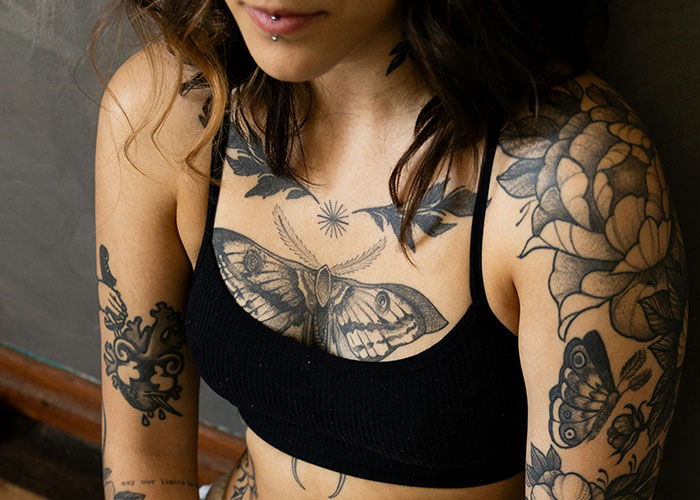 Woman with multiple tattoos on arms and chest wearing a black top, illustrating safety tips women picked up for self-protection.