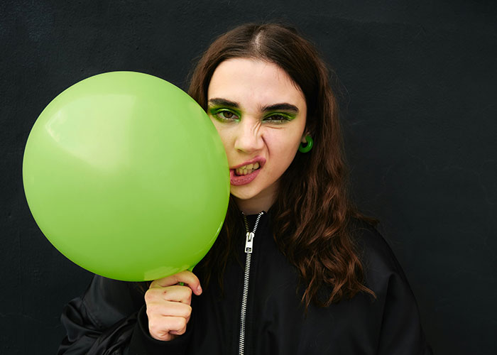 Young woman with green eye makeup holding a green balloon, representing safety tips women picked up hard way.