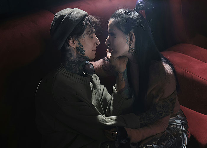 Two tattooed women share an intimate moment on a red couch illustrating safety tips women picked up the hard way.