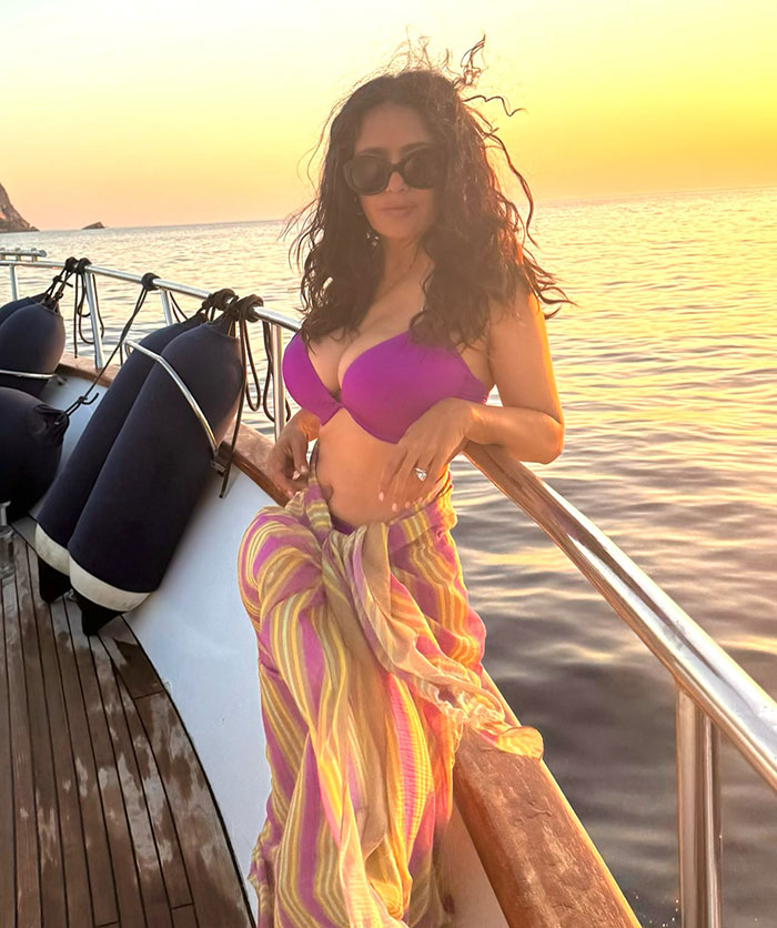 Salma Hayek in purple bikini top and striped sarong posing on boat at sunset for Sports Illustrated Swimsuit cover.