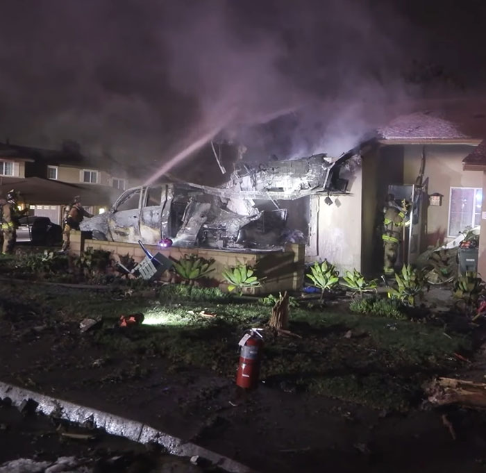 Firefighters spray water on the wreckage of a house after a San Diego plane crash involving a famous drummer.