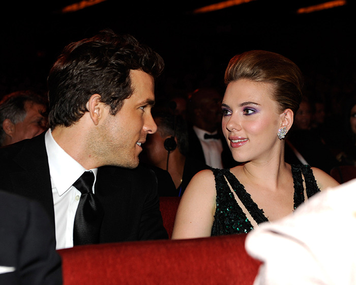 Scarlett Johansson and Ryan Reynolds in formal attire seated and conversing at an indoor event with dim lighting.