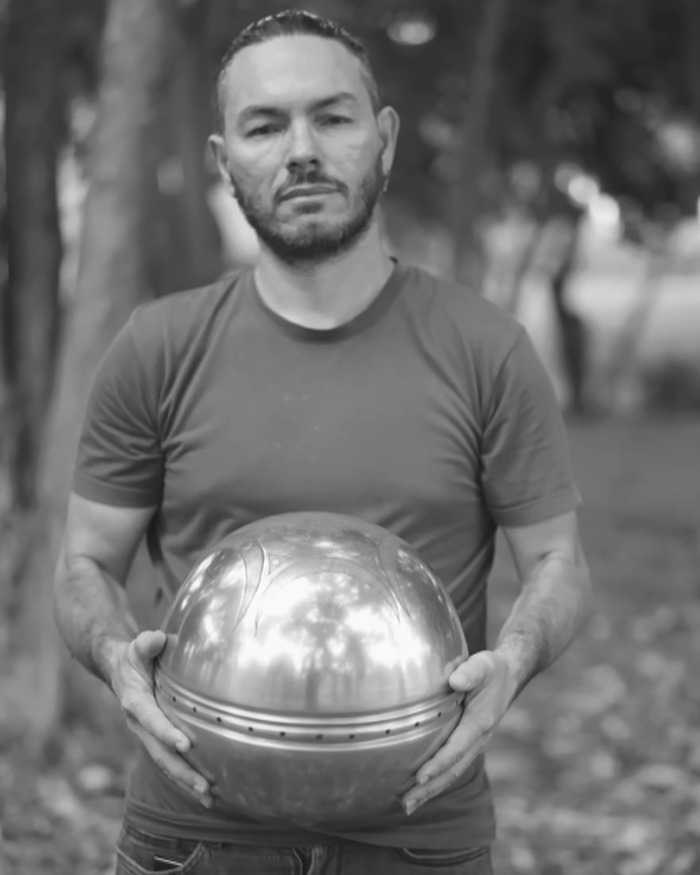 Man holding a metallic UFO with ominous inscriptions about origin of birth in an outdoor setting with trees in background