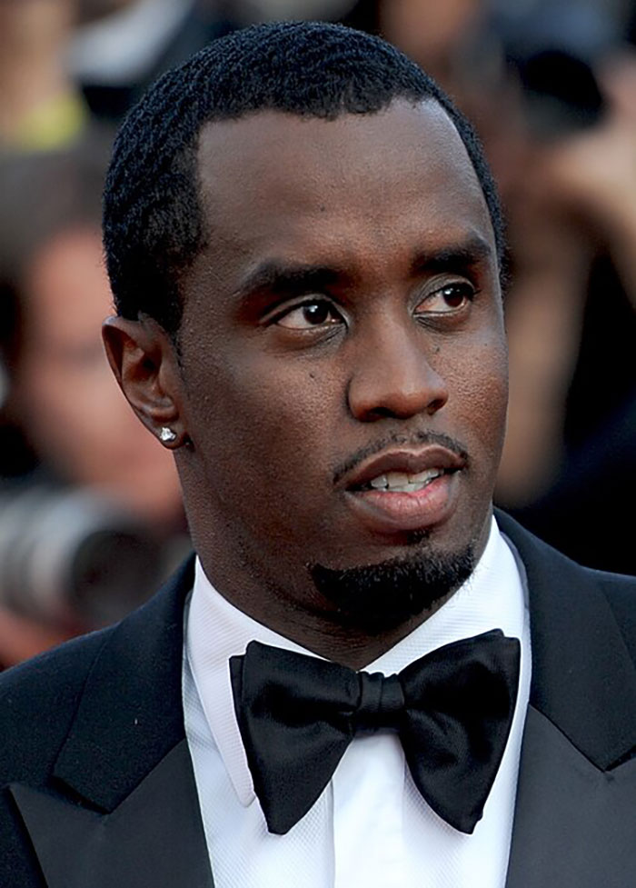 Diddy wearing a tuxedo and bow tie, attending an event while on the stand during a graphic freak-offs description.