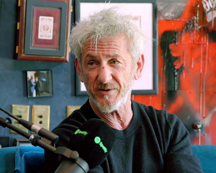 Sean Penn with a rough appearance speaking into a podcast microphone discussing his heavy claims about Woody Allen.