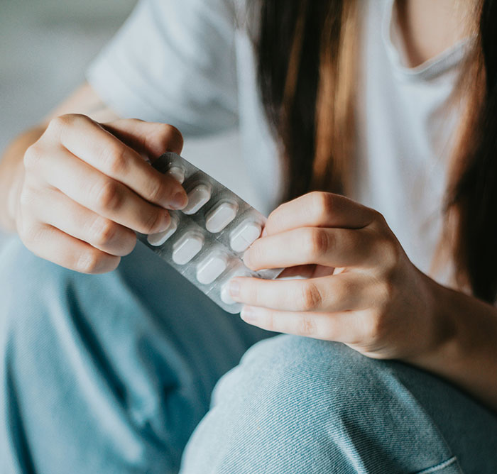 Person holding a blister pack of pills, highlighting symptoms that require immediate medical attention.