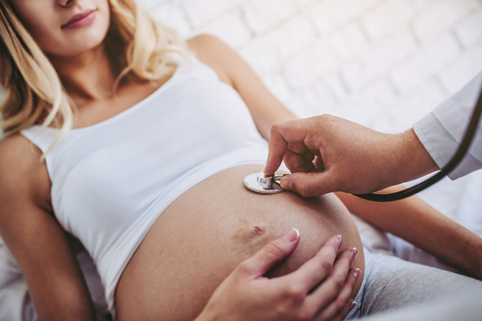 Pregnant woman being examined with a stethoscope illustrating symptoms that require immediate medical attention.