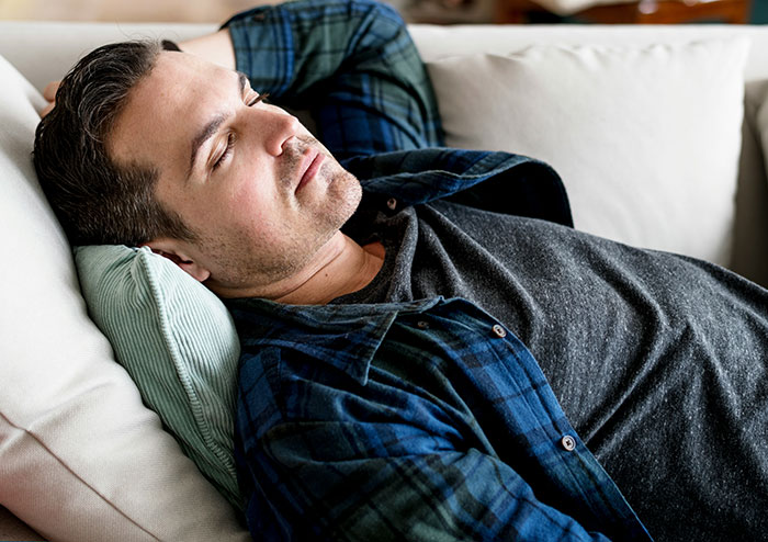 Man lying on couch with eyes closed, appearing fatigued, illustrating symptoms that may require immediate medical attention.