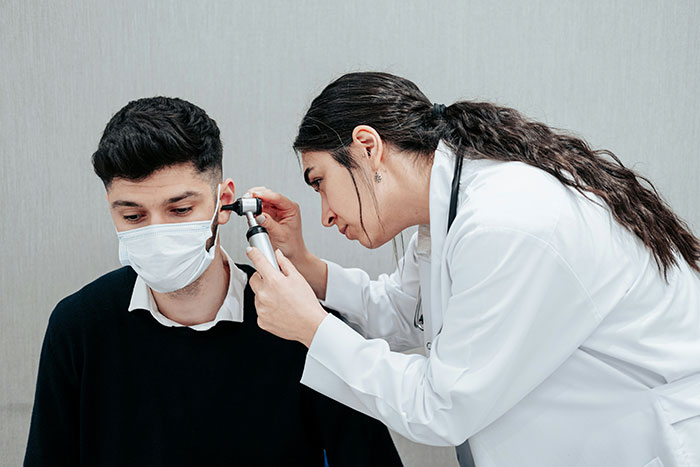 Doctor in white coat examining patient's ear with otoscope, highlighting symptoms that require immediate medical attention.