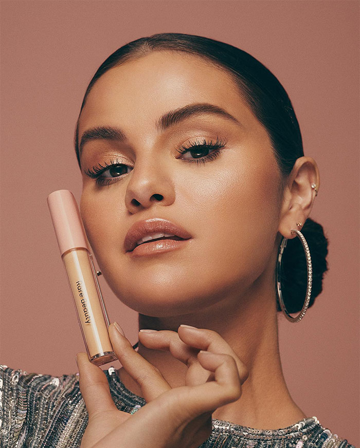 Selena Gomez showcasing makeup product in a close-up portrait highlighting her net worth from beauty earnings.