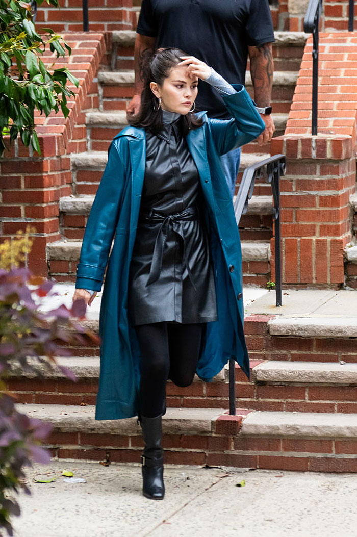 Selena Gomez walking outdoors in stylish leather outfit and teal coat, highlighting her net worth makeup earnings in 2025.