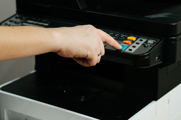 A hand pressing the start button on a printer control panel, illustrating moments of unexpected stupidity.