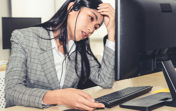 Woman in a gray plaid blazer wearing headset, looking frustrated at computer, illustrating moments of people being so stupid.