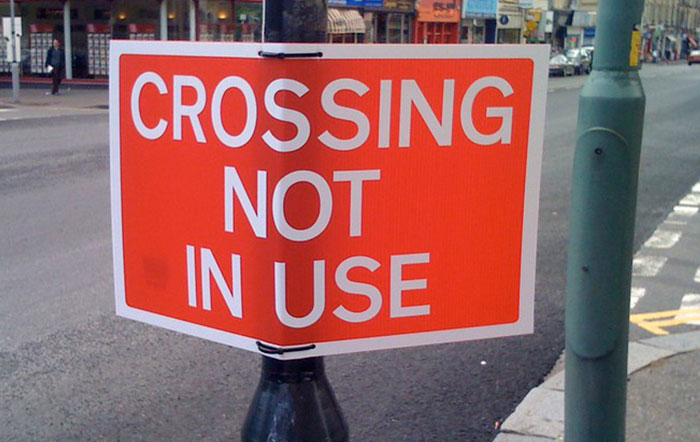 Orange sign on street stating crossing not in use, showcasing an example of surprising moments of people being so stupid.